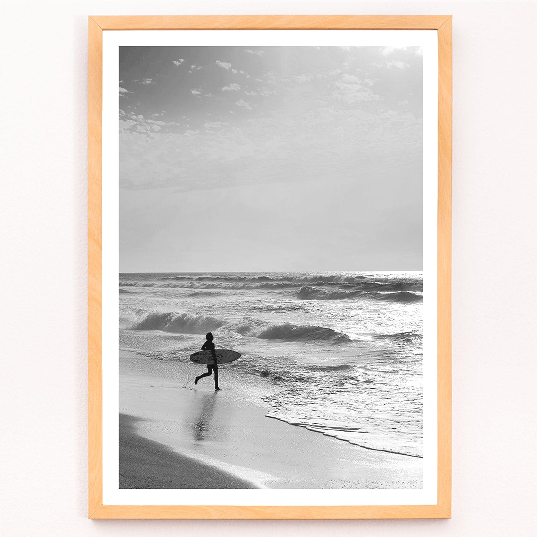 Black and white poster of a surfer with a board entering the ocean titled Surfer in Portugal by artist Black, framed and displayed in modern living room decor