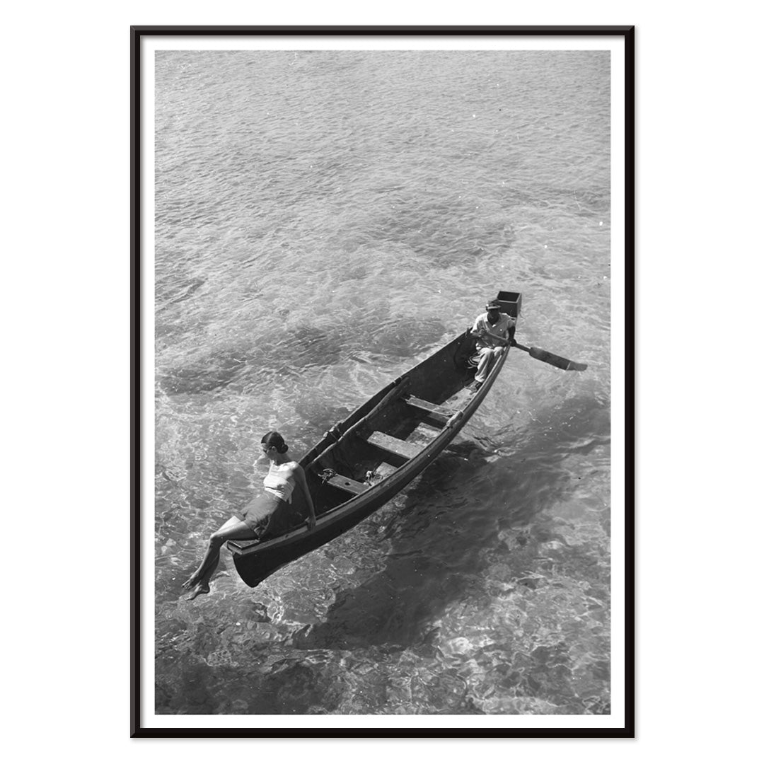 Fashion model on boat edge with man rowing in clear water Montego Bay Jamaica by Toni Frissell artwork poster, with black aluminium frame on white background