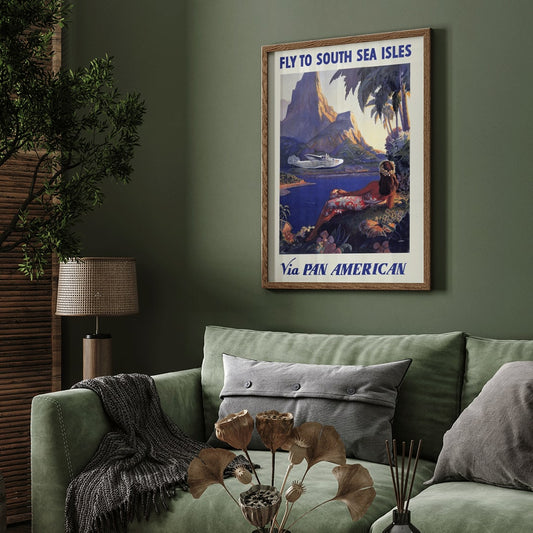 Vintage travel poster of a woman in a floral dress on a tropical island with a Pan American seaplane by Paul George Lawler, framed and displayed in home decor