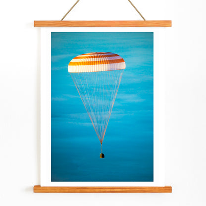 Soyuz TMA-14M spacecraft descending with parachute against blue sky NASA Expedition 42 landing poster artwork, with wooden magnetic frame on white background