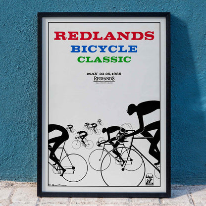 Cyclists racing illustration and poster by Karlis Smiltens titled Redlands Bicycle Classic featuring red blue and green text on white background, framed and displayed in home decor