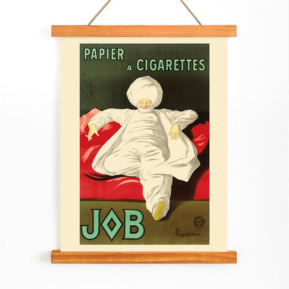 Cigarette Rolling Paper Job poster by Leonetto Cappiello showing a relaxed man in white robes and turban reclining with a cigarette on a red couch, with wooden magnetic frame on white background